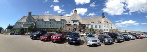 A large lodge with a stone facade and multiple cars parked in front, set against a blue sky with scattered clouds.