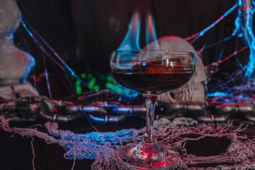 A flaming cocktail in a glass, surrounded by spider webs and a skull, creating a spooky atmosphere.