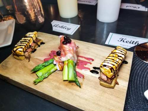 A gourmet dish featuring grilled meat, asparagus, and sauces, presented on a wooden board.
