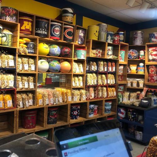 A colorful display of popcorn in various containers and themed buckets on wooden shelves in a shop.