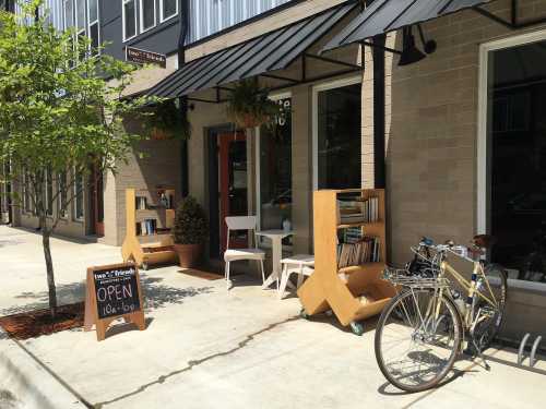 A cozy storefront with bookshelves, a small table, a bike, and an "OPEN" sign on the sidewalk.