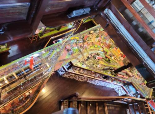 Aerial view of a detailed model train layout with tracks, buildings, and vehicles, seen from a staircase.