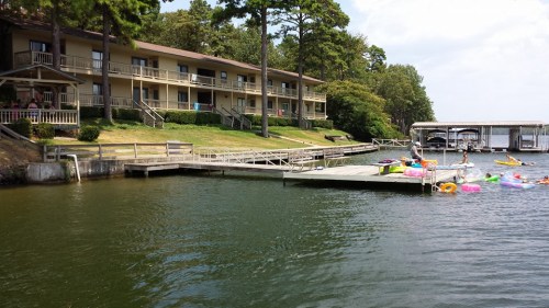 A lakeside scene featuring a two-story building, a dock, and colorful inflatable rafts on the water.