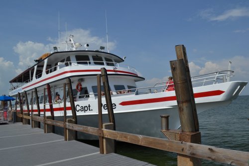 A large white and red boat named "Capt. Lee" docked at a wooden pier on a calm waterway under a blue sky.