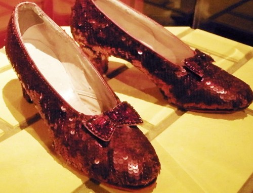 A pair of vintage red sequined shoes with a small bow on each, displayed on a yellow surface.