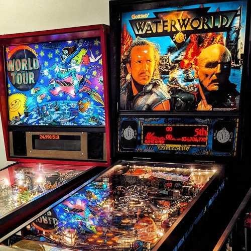 A close-up of two pinball machines: "World Tour" on the left and "Waterworld" on the right, featuring vibrant artwork.