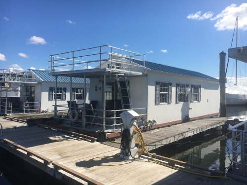 A dock with a white building and a blue roof, surrounded by water and boats under a clear blue sky.