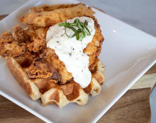 A plate featuring crispy fried chicken on a waffle, topped with creamy sauce and garnished with fresh herbs.