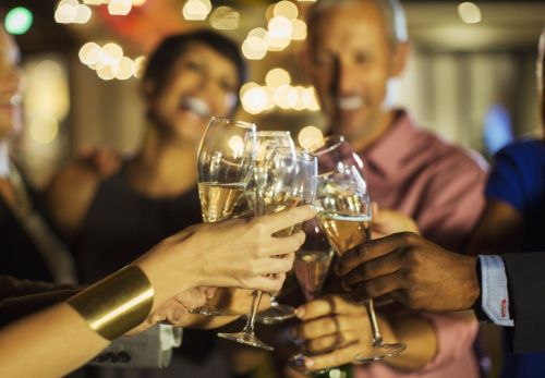 A group of people toasting with glasses of champagne in a festive setting with soft lights in the background.