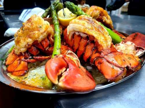 A platter of grilled lobster tails and claws, garnished with asparagus and lemon, served on a silver tray.