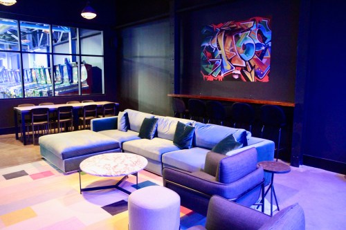 A modern lounge area with a blue sofa, colorful rug, and a vibrant graffiti artwork on the wall.