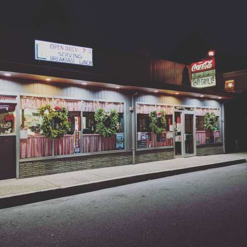 A cozy diner at night, featuring festive wreaths on the windows and a vintage Coca-Cola sign.