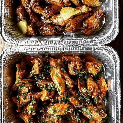 Two trays of chicken wings: one with a glossy sauce and green onions, the other with a sweet glaze and pineapple.