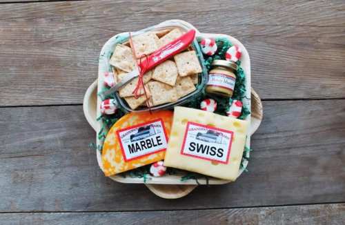 A wooden platter with assorted cheeses, crackers, and a jar of honey, decorated with festive red and white accents.