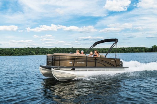 A pontoon boat with three people cruising on a lake under a blue sky with fluffy clouds.