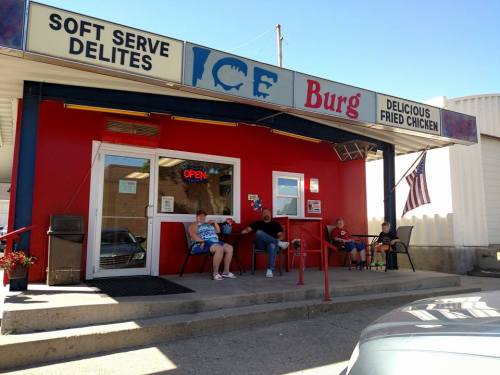 A colorful fast-food restaurant with a sign for soft serve and fried chicken, featuring people sitting outside.