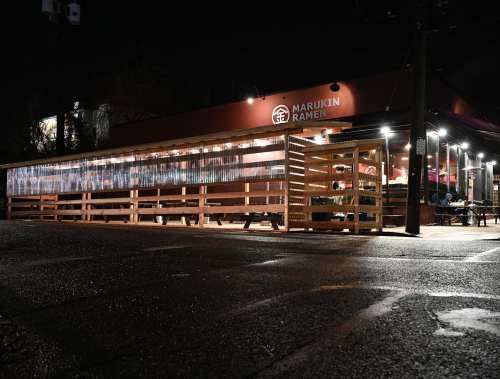 A nighttime view of Marukin Ramen, featuring outdoor seating and illuminated windows.