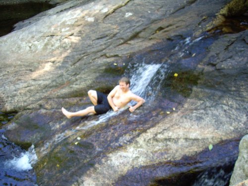 A person relaxes on a rocky surface near a small waterfall, enjoying the natural surroundings.