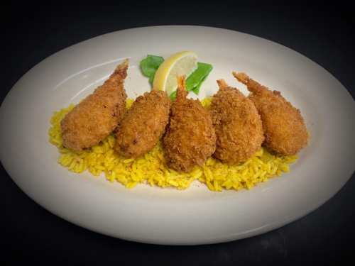 Five golden-brown fried shrimp on a bed of yellow rice, garnished with a lemon wedge and a basil leaf.