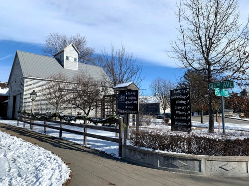A snowy scene featuring a rustic building with signs for lodging, dining, and shops, set against a clear blue sky.