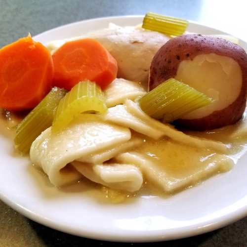 A plate of chicken and dumplings with carrots, celery, and purple potatoes.