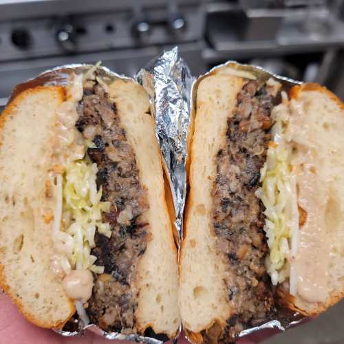 A close-up of a halved sandwich with a thick patty, shredded cabbage, and sauce, wrapped in foil.