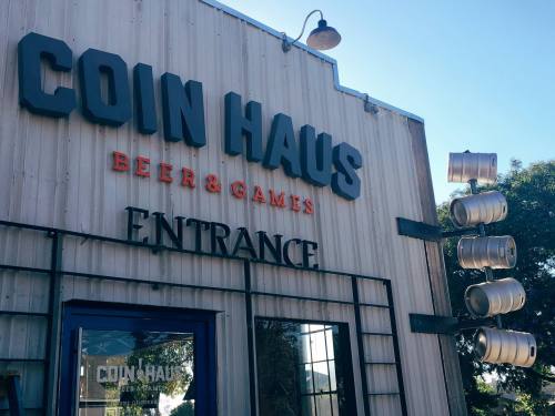 Signage for "Coin Haus Beer & Games" with an entrance and decorative beer kegs on the exterior.