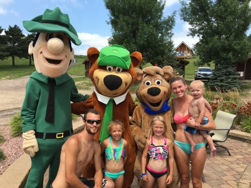 A family poses with two cartoon mascots at a poolside, smiling and enjoying a sunny day.