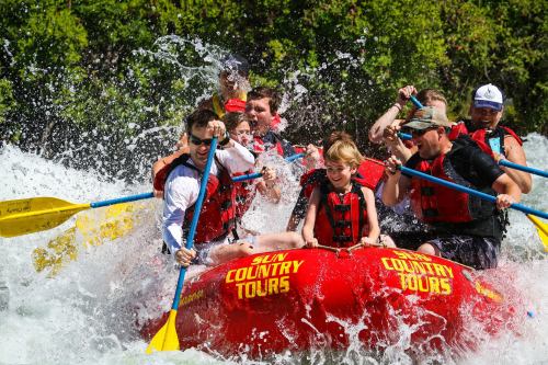 A group of people in red life jackets enjoying white-water rafting, splashing water around them.