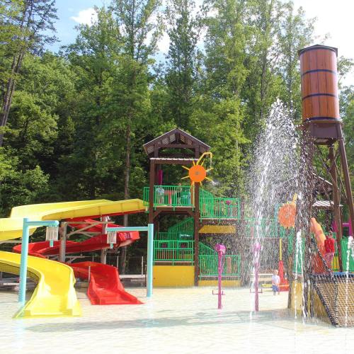 Colorful water slides and play structures in a splash park surrounded by trees on a sunny day.