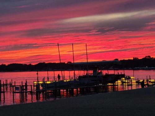 A vibrant sunset paints the sky in shades of pink and orange over a calm lake, with silhouettes of boats and docks.