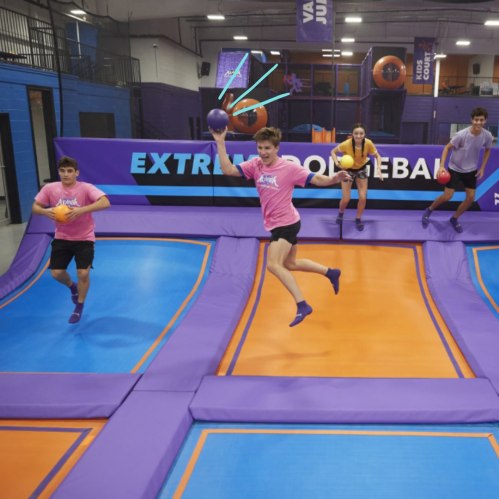 A group of kids playing extreme volleyball on trampolines, smiling and holding balls in a colorful indoor arena.