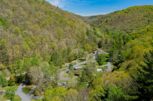 Aerial view of a lush green valley with winding roads and RVs nestled among trees in a serene landscape.