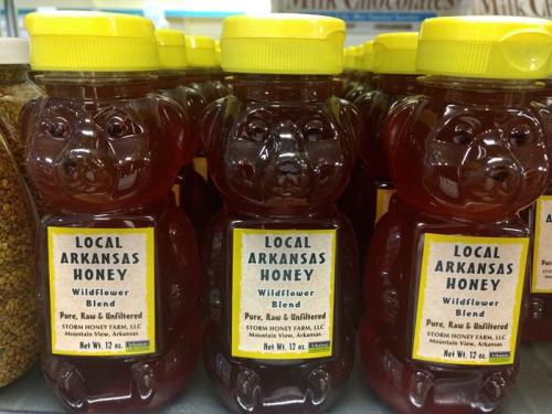 Three bear-shaped bottles of local Arkansas wildflower honey, labeled "Pure, Raw & Unfiltered," on a store shelf.