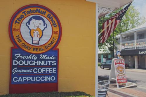 Colorful storefront of The Tatonut Shop, featuring a sign for doughnuts, coffee, and cappuccino. Open for business.