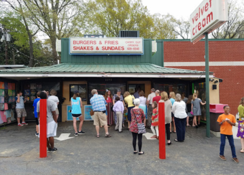 A busy burger and fries restaurant with a crowd outside, featuring a sign for shakes and sundaes.