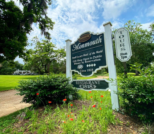 Sign for Monmouth, a luxury hotel with a gift shop, dining by reservation, and tour information, surrounded by greenery.