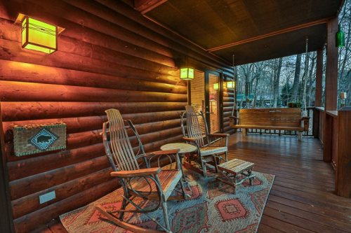 Cozy porch with wooden rocking chairs, a small table, and warm lighting, surrounded by trees.