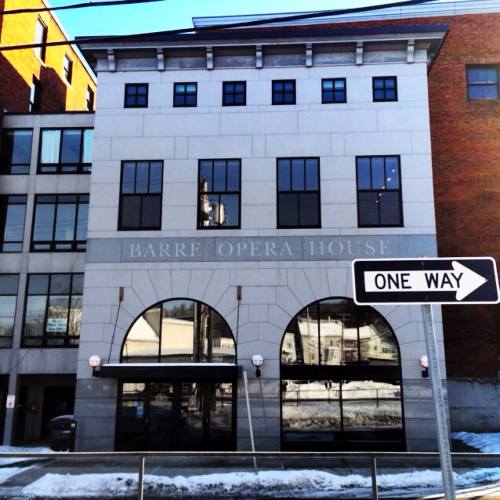 Exterior of Barre Opera House with large arched windows and a "One Way" street sign in front. Snow on the ground.
