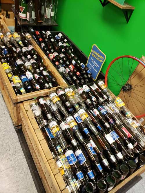 A display of various beer bottles arranged in wooden crates against a green wall.