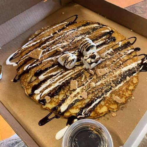 A large pancake topped with chocolate and marshmallow drizzles, crushed graham crackers, and mini marshmallows in a box.