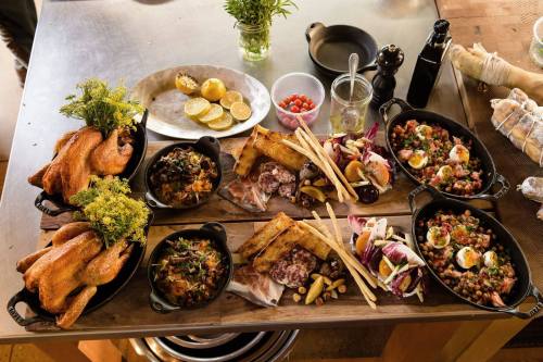 A table spread with various dishes, including roasted chickens, salads, and sides, garnished with herbs and lemon.