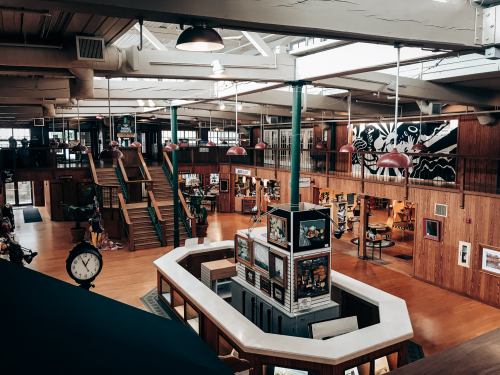 A spacious, well-lit interior of a creative space with wooden walls, art displays, and a central staircase.