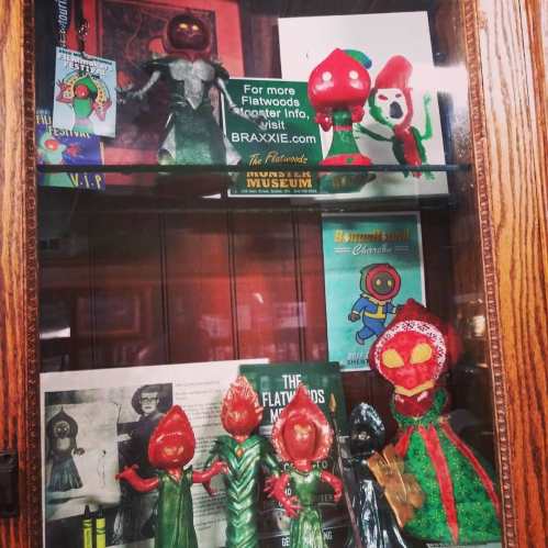 Display case featuring colorful, whimsical figures and memorabilia related to Flatwoods Monster lore.