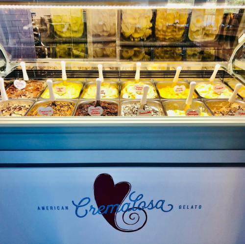 A display of various gelato flavors in a shop, with colorful tubs and a sign reading "Cremalosa American Gelato."