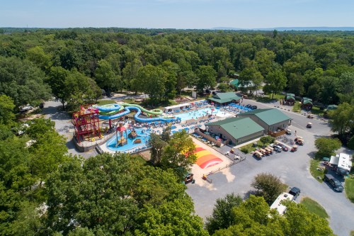 Aerial view of a water park with slides, pools, and green trees surrounding the area.