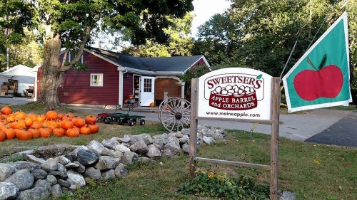 A red barn with pumpkins in front, a sign for Sweetiser's Apple Barrel and Orchards, and a green flag with an apple.