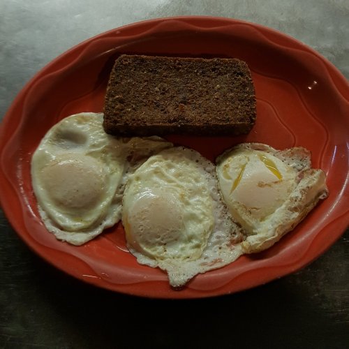 A red plate with two fried eggs and a slice of dark bread.