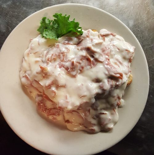 A plate of food featuring a creamy sauce over sliced meat, garnished with a leaf of lettuce.