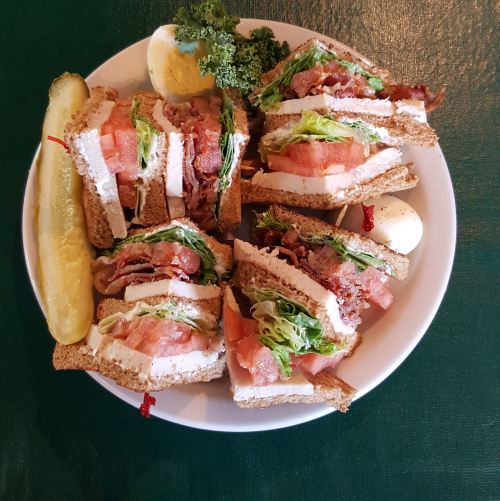 A plate of stacked sandwiches with bacon, lettuce, tomato, and turkey, accompanied by a pickle and a hard-boiled egg.